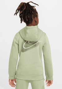 Hanorac verde cu glugă, cu manșete și tiv elastice, având un logo Nike mare alb pe spate cu un design de gradient în dungi.