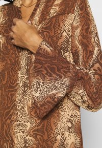 Braun und creme gemusterte Bluse mit lockerer Passform, die ein weit ausgestelltes Bündchen und eine subtile Textur aufweist, geeignet für die Freizeit.