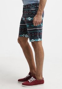 Pánské plavky černé barvy s geometrickými vzory v tyrkysové, bílé a burgundské; vyrobené z lehkého materiálu; boční kapsy; do délky kolen.