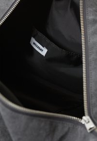 Interno di una borsa in tessuto nero con un'etichetta bianca visibile che recita "WEEKDAY". Presenta cuciture grigie e una chiusura con zip argentata.