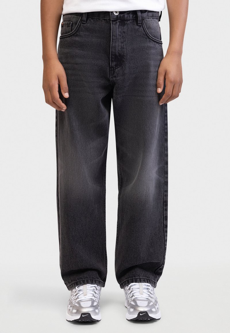 Jeans negri din denim, cu croială lejeră și decolorare subtilă. Dispune de cinci buzunare și închidere cu nasture. Asortat cu adidași gri.