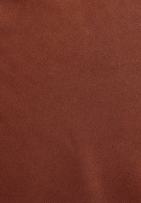 Rūsu krāsas audums ar diagonālu twill auduma rakstu, rādot tuvumā tekstūru un smalkās šķiedras.