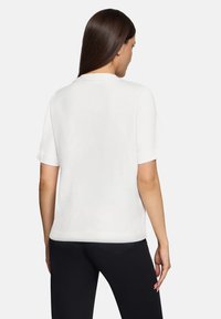 Hvid kortærmet skjorte med rund hals, glat tekstur og afslappet pasform, parret med sorte bukser synlige ved hoftene.