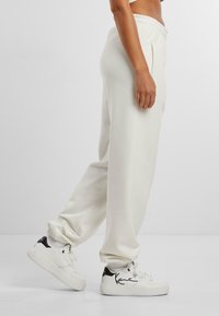 Hvide, løstsiddende sweatpants med elastisk talje og sidelommer. Sammen med hvide sneakers med sorte detaljer.