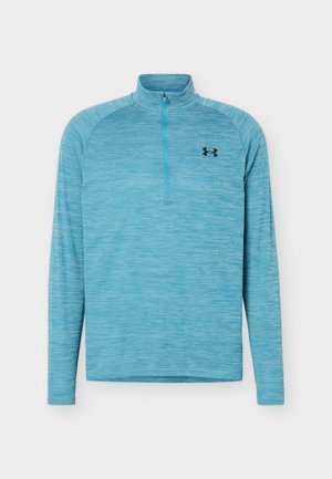 Jasnoniebieska męska bluza z długim rękawem, z ćwiartkowym zamkiem błyskawicznym i czarnym logo Under Armour na lewej piersi.