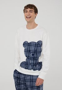 Biała koszulka z długim rękawem z dużym graficznym wzorem niebieskiego misia w kratę. Wygodny krój z miękkiego materiału; w zestawie z dopasowanymi spodniami w kratę.