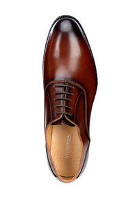 Zapato de vestir de cuero marrón con textura suave, que presenta una puntera redondeada, diseño con cordones y sutiles detalles de costura. En el interior se muestra el nombre de la marca "WITTCHEN."