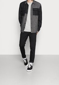 Sort og grå skjorte med knapper og to forlommer, kombineret med mørke bukser og sorte sneakers med hvide såler samt grå sokker.