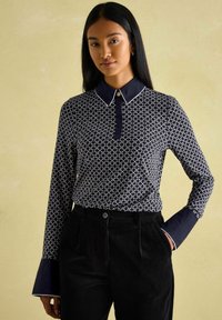 Marinebluse mit langen Ärmeln und festem Kragen, ausgestattet mit einer Knopfleiste und Kontrastbesatz an den Manschetten und dem Kragen.