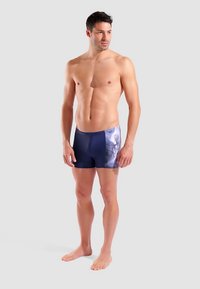 Navyblaue Badeshorts mit einem dynamischen Grafikdesign in verschiedenen Blautönen und hellen Akzenten, gefertigt aus einem glatten, dehnbaren Stoff.