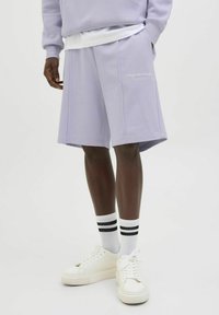 Lila shorts i mjukt tyg, med sidofickor och broderad "Originals Studio" logotyp. Kombineras med vita sneakers och randiga strumpor.