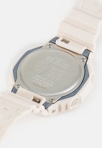 Light pink silicone watch strap with a silver stainless steel back, featuring engraved details and blue accents around the case.