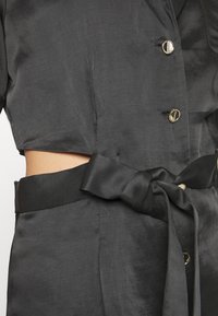 Robe en satin noir avec un devant boutonné, des manches courtes, une ceinture nouée à la taille et une découpe latérale pour un design supplémentaire.