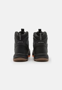 Pari mustia korkeavartisia urheilu kenkiä ruskeilla pohjilla, tekstuurissa oleva kangas ja vetonauhat nähtynä takaa valkoista taustaa vasten.