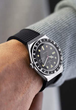 Quartz wristwatch with a black dial, luminous hour markers, stainless steel case, and black patterned silicone strap. Date display at 3 o'clock.