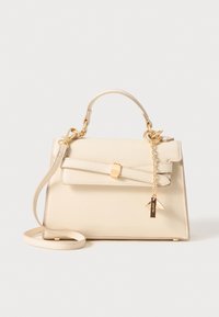 Bolso de mano color crema hecho de material sintético, con un asa superior, correa de hombro desmontable, detalle de lazo y herrajes en tono dorado.