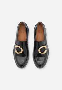 Mocassins en cuir verni noir avec un accent circulaire en or sur l'empeigne et une semelle intérieure en cuir marron. Design à bout arrondi et semelle épaisse.