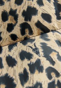 Leopardmønstret stof med beige og sorte pletter, der har et subtilt grafik af et geddehoved. Glat tekstur og mønstret design.