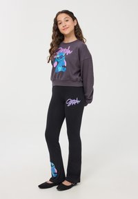 Czarne leginsy z niebieską grafiką Sticha na kostce, w zestawieniu z szarym swetrem z motywem Sticha i fioletowym napisem.