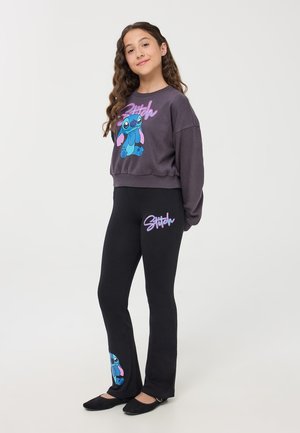 Leggings neri con una grafica blu di Stitch all'altezza della caviglia, abbinati a un sweatshirt grigio con un disegno di Stitch e scritte viola.