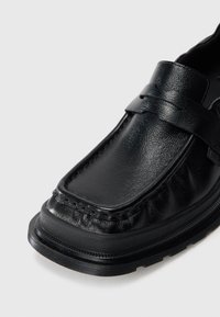 Sorte skinnloafers med teksturert finish, med en sydd design og flat gummisål. Utsmykket med et belte over forsiden.