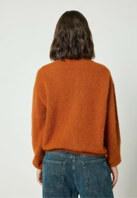 Rostpunane kootud sviiter, millel on vabalt langev lõige, soonikud varrukatel ja tekstuur, koos siniste teksadega, millel on tagataskud.