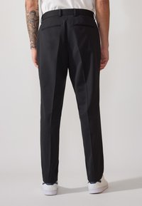 Pantaloni negri cu o croială adaptată, având două buzunare la spate și o textură netedă. Purtați cu pantofi sport albi.