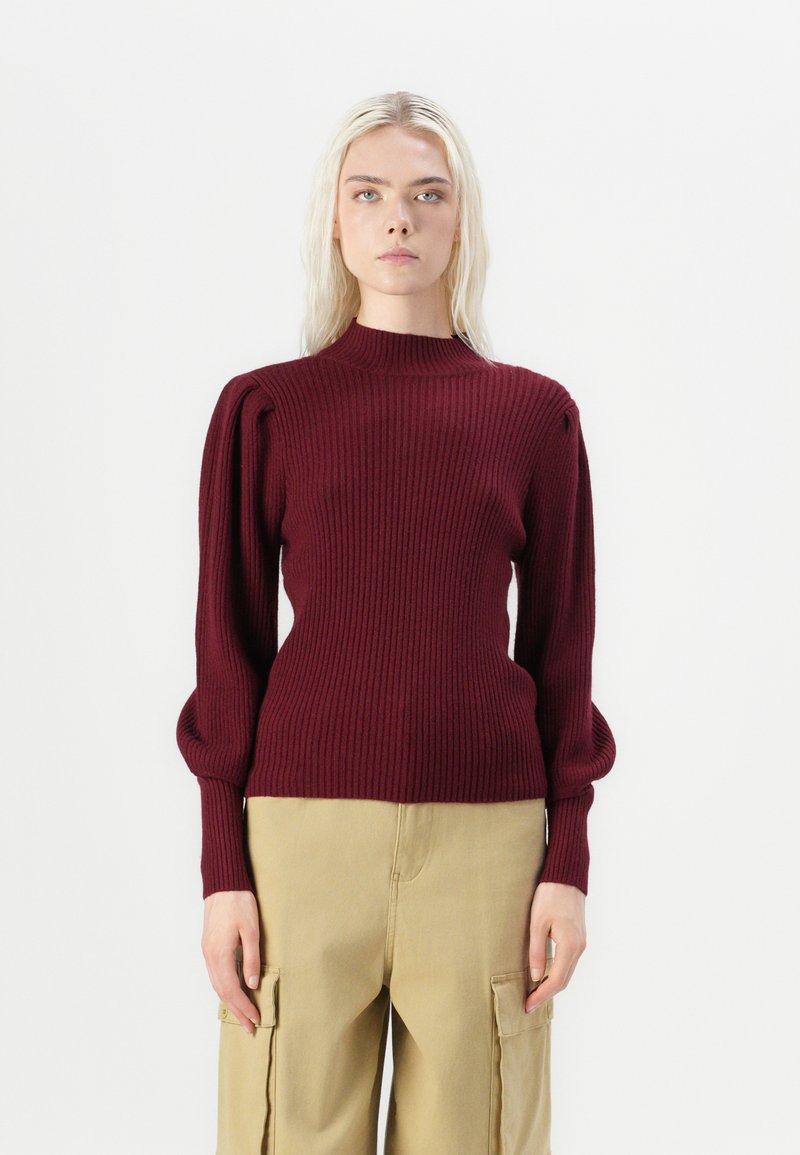 Burgundy ribbed knit sweater with a high neck, round shoulders, and puffed sleeves, paired with beige cargo pants, featuring side pockets.