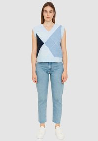 Maglione senza maniche in azzurro chiaro con scollatura a V e motivo a rombi, caratterizzato da diamanti blu scuro e navy. Abbinato a jeans azzurri chiari e sneakers bianche.