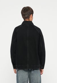 Black denim jacket with a collar, raglan sleeves, and visible stitching details. Smooth texture, relaxed fit, and buttoned cuffs.