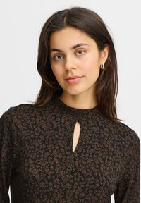 Juoda bluzonėlė su rudos spalvos lapų raštu, raktų formos iškirpte, ilgiems rankovėms ir glotnia tekstūra. Nėra puošmenų ar metalinių detalių.