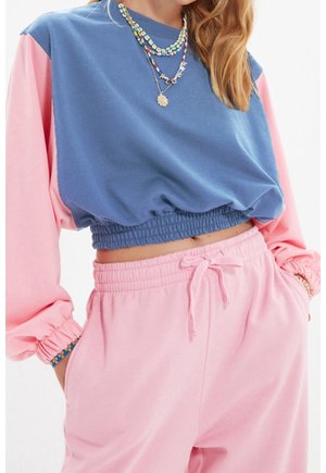 Crop top en color block bleu et rose, avec un ourlet élastique et des manches bouffantes. Pantalons de survêtement roses assortis avec taille à cordon.