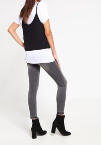 Camiseta de tirantes negra sobre una camiseta blanca, combinada con jeans ajustados grises y botas de ante negras hasta el tobillo, con tacón cuadrado.