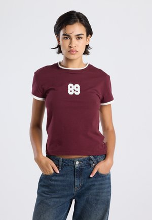 Bordeaux T-shirt met korte mouwen en witte afwerking, met een nummer "89" aan de voorkant. Gemaakt van stof met een gladde textuur.