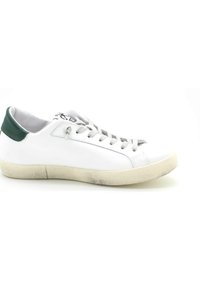 Sneaker in pelle bianca con un accento verde sul tallone, lacci grigi, suola in gomma bianca e lievi segni di usura sulla suola.