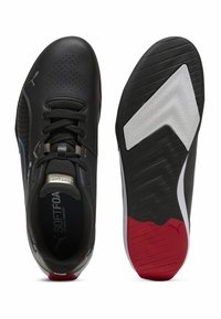 Černé atletické boty s hladkým koženým svrškem, síťovými detaily a texturovanou gumovou podrážkou se červenými a bílými prvky.