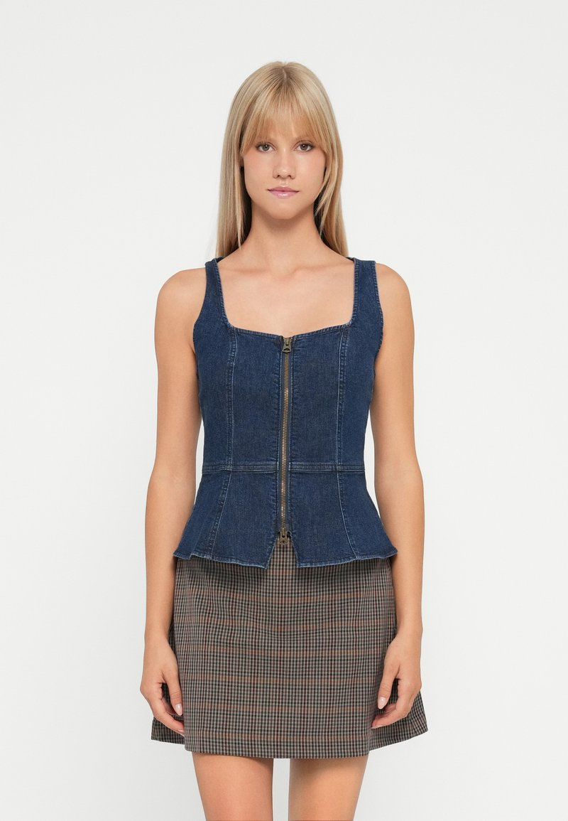 Denim peplum top with square neckline and front zipper, featuring a dark blue color and structured design. Paired with a plaid skirt.