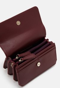 Portafoglio in pelle bordeaux con chiusura a pressione, dotato di più compartimenti con zip e una finitura testurizzata. Dettagli in hardware color oro.