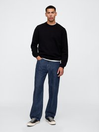 Schwarzer Rundhalsausschnitt-Sweatshirt aus weichem Stoff, kombiniert mit blauen Jeans im Straight-Leg-Schnitt. Die Sneaker verfügen über ein Schwarz-Weiß-Farbdesign.
