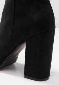 Sorte ankelstøvler med høje hæle, lavet af ruskind. Har en kraftig blokhælsåle og en glat overflade med minimalistiske designelementer.