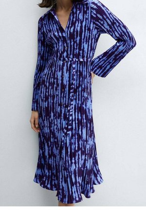 Frau trägt ein langärmeliges, geknöpftes Kleid mit blauem und dunkelviolettem Tie-Dye-Muster, mit Kragen und Taillengürtel.