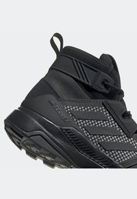 Černé turistické boty s prodyšným svrchním materiálem, texturovanou gumovou podrážkou a zesíleným opatkem. Obsahují poutko na patě a decentní branding.