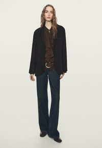 Czarna marynarka z miękkiej tkaniny, brązowa warstwowa bluzka z falbanami, ciemne dzwoniaste dżinsy oraz brązowe botki na obcasie. Prosty i uporządkowany fason.