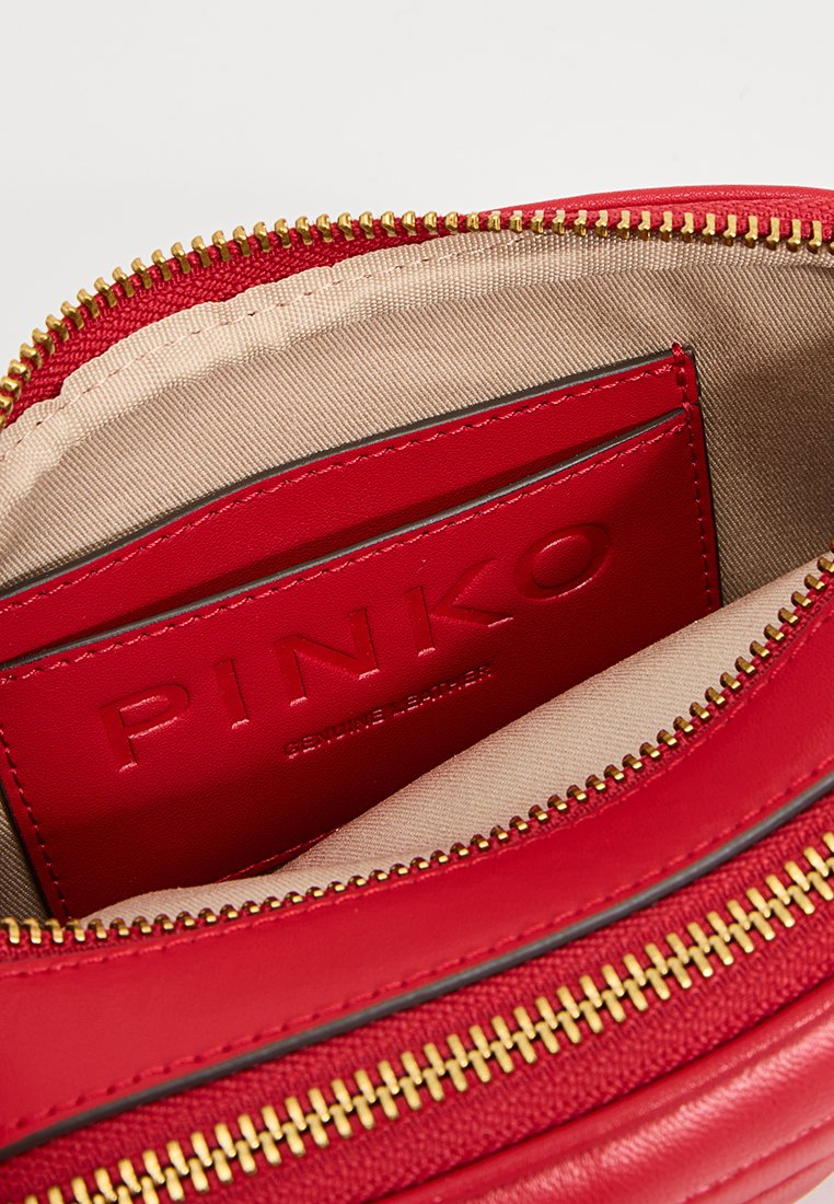 Intérieur d'un sac en cuir rouge avec une fermeture éclair dorée, une doublure en tissu beige et une poche pour cartes embossée du marquage "PINKO" attestant du cuir véritable.