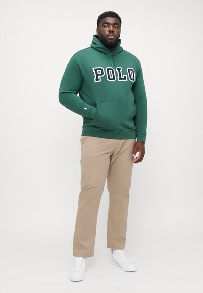 Felpa verde con grande lettering bianco "POLO", tasca a marsupio, abbinata a pantaloni beige e sneaker bianche. Tessuto liscio, design casual.