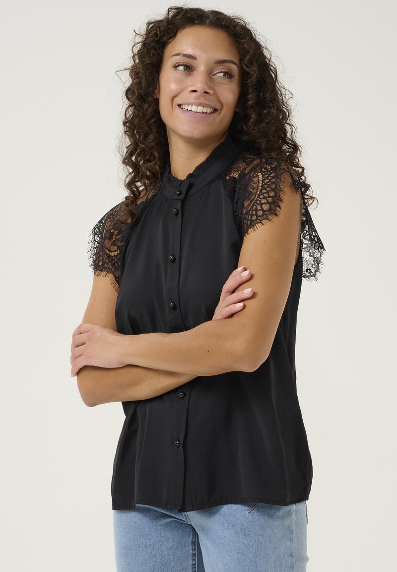 Black short-sleeve blouse with lace accents, button front, and collar. Soft texture, slightly loose fit. Worn with light blue jeans.