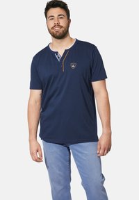 Navy blue short-sleeve T-shirt with a buttoned Henley neck, a contrasting orange accent, and embroidered emblem on the chest.