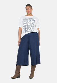 Witte t-shirt met een zwart abstract lijnontwerp, gecombineerd met marineblauwe wijde broek en bruine cowboylaarzen. Soepele stof, normale pasvorm.