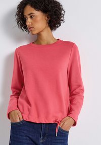 Koraalroze sweatshirt met een ronde hals, lange mouwen en een trekkoorddetail aan de onderkant. Zachte stof met een gladde textuur.