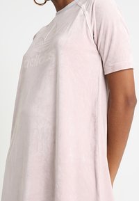 Różowa, luźna sukienka-tee z bawełny z krótkimi rękawami, z tonalnym logo Adidas z przodu i subtelnymi detalami tekstury.